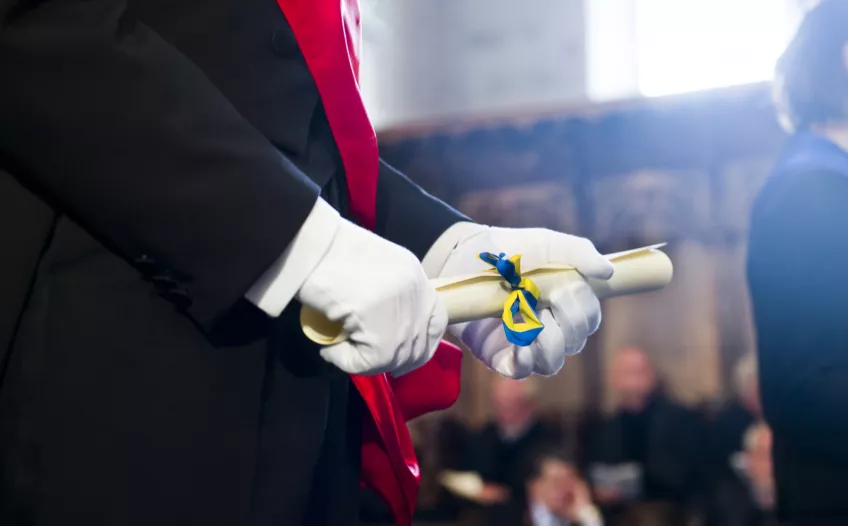 Nybliven doktor håller sitt diplom i händerna. Foto. 